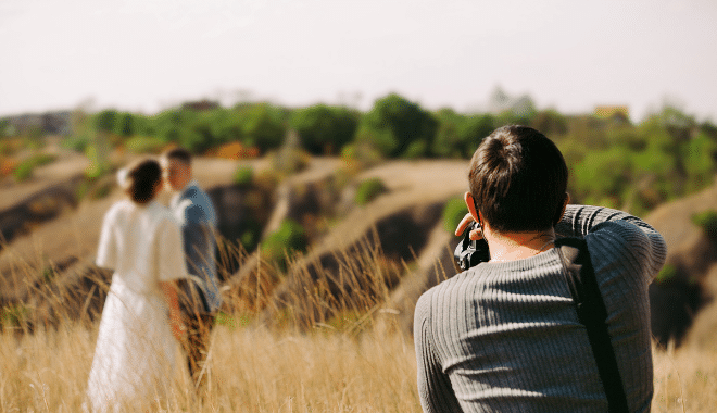 photographe prenant en photo des mariés dans un champ
